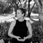 czarnobiała fotografia kobiety, w ciemnym podkoszulku,w dłoniach trzyma telefon komórkowy i patrzy lewo. Jest to Katarzyna Czachowska